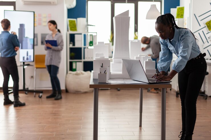 architect-modern-achitectural-office-working-laptop-desk-with-3d-white-foam-scale-model-skyscraper-engineer-looking-blueprints-architecture-project-urban-development-area_482257-33561.jpg