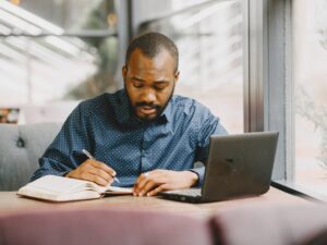 african-american-man-working-laptop-writing-notebook-man-with-beard-sitting-cafe.jpg